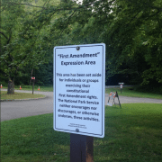 A photo of the "First Amendment Sign" at a National Park. The sign says "First Amendment Expression Area: This area has been set aside for individuals or groups exercising their constitutional First Amendment rights. The National Park Service neither encourages nor discourages, or otherwise endorses, these activities."