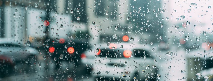 A close up of rain on a window with cars blurred in the background