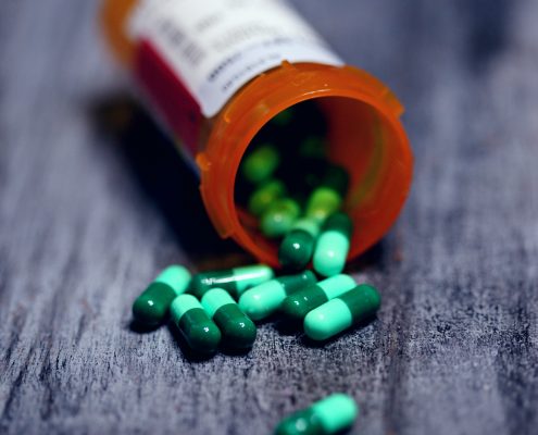 A pill bottle with green pills spilling out