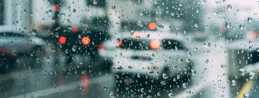 A close up of raindrops on a window with blurred cars in the background