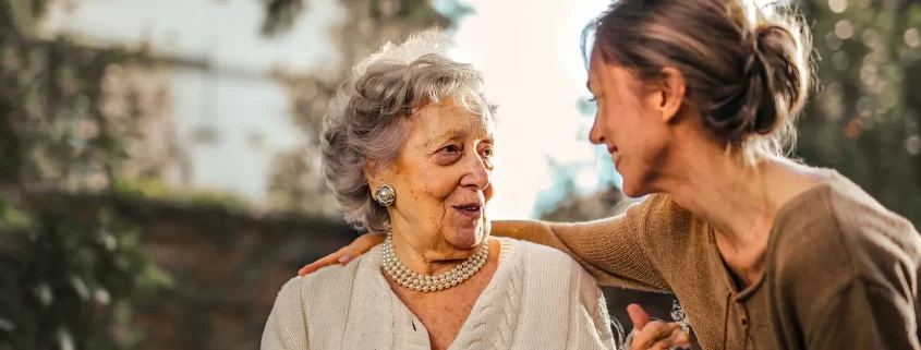 An adult woman holding the hand of her elderly mother