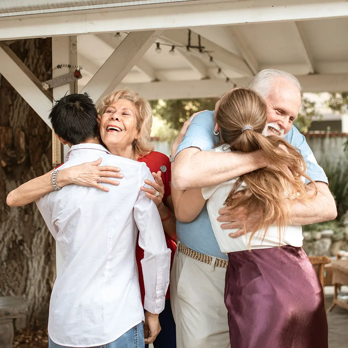 Two elderly parents hugging their adopted adult children