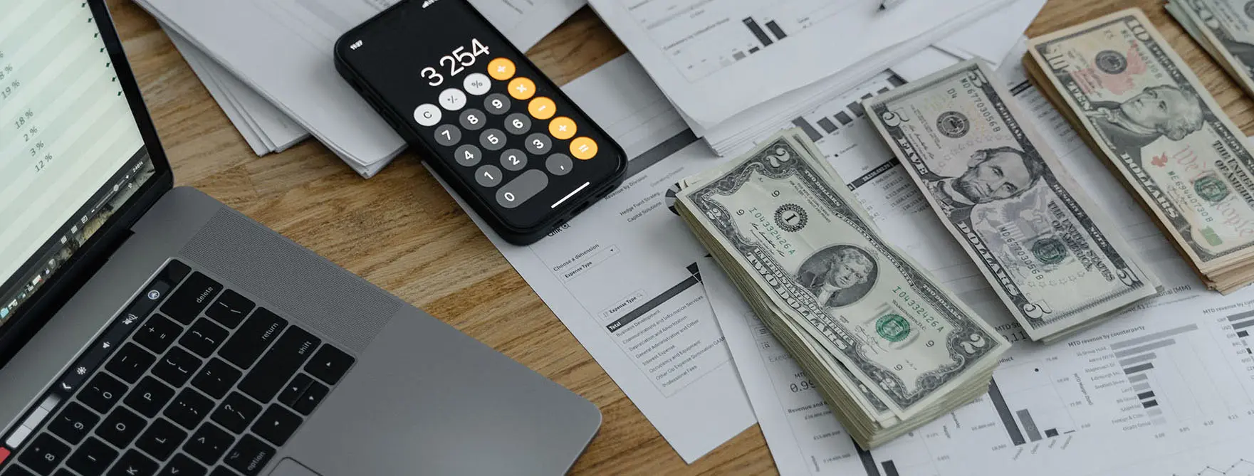 A computer, financial paperwork, piles of cash, and an iPhone calculator