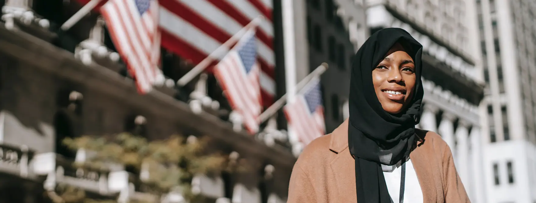 A young immigrant woman smiling outside of a building with American flags