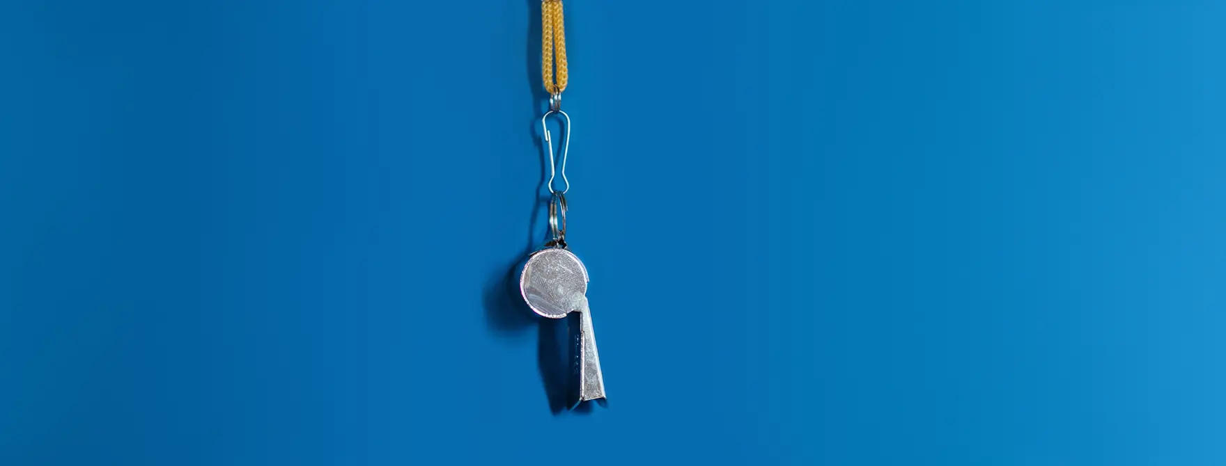 A silver whistle hanging on a yellow string in front of a blue background