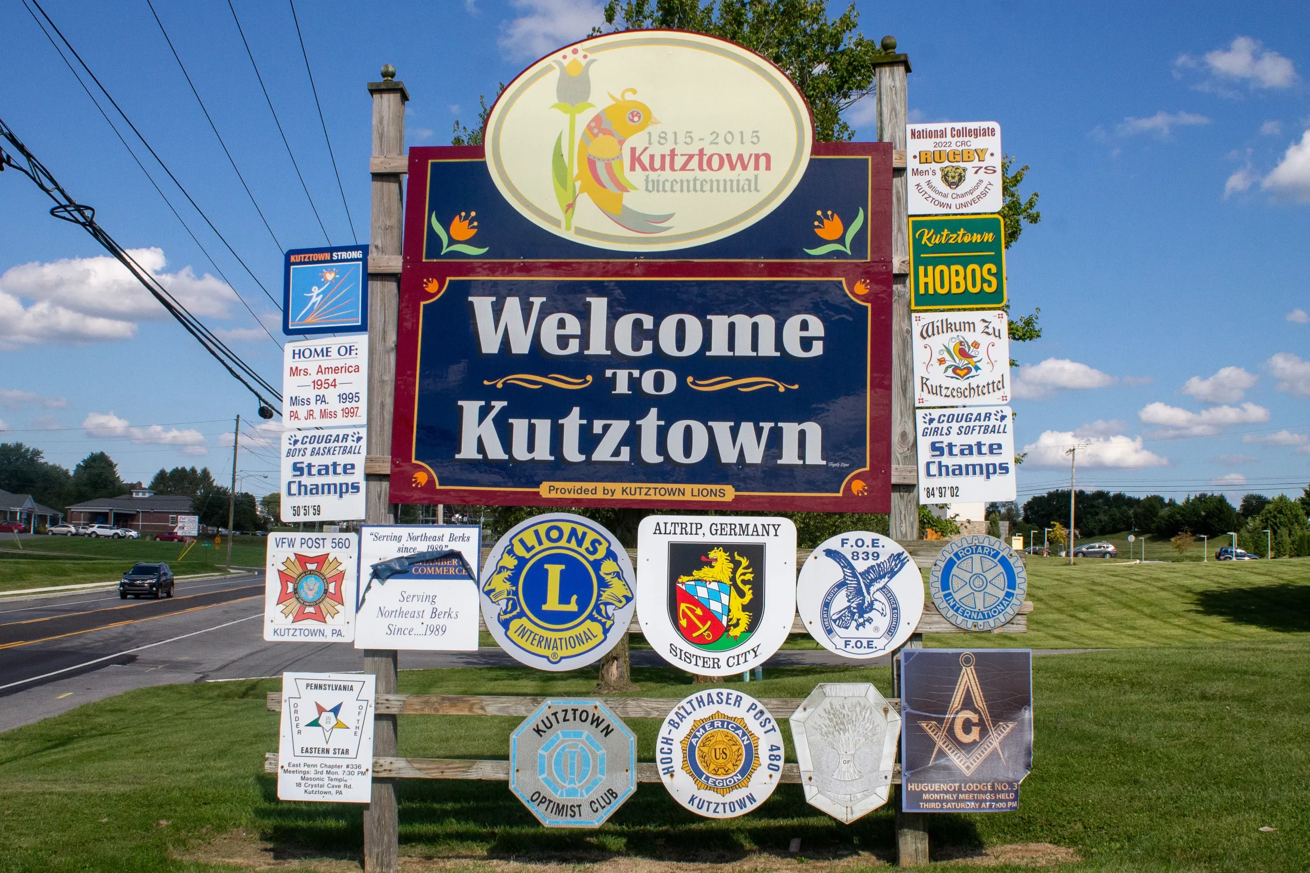 A photo of the Welcome to Kutzown sign, surrounded by smaller signs showcasing different clubs and championships from the area.