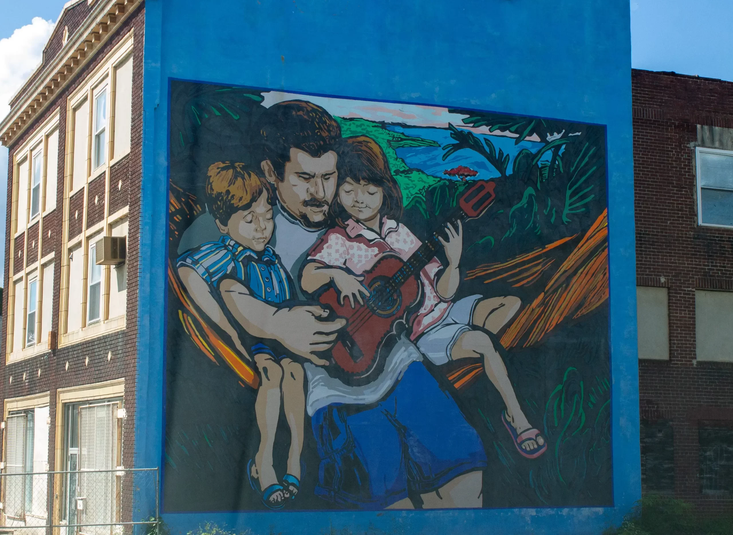 A mural of a father playing guitar with his two children painted on the side of a building in Reading.