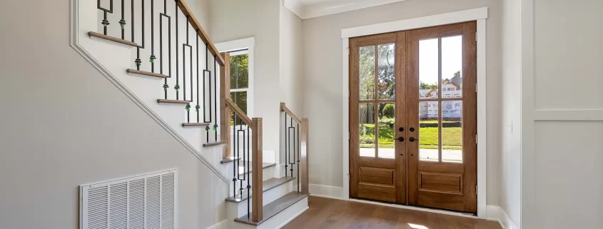 The inside of a home's front room. There is a staircase and a set of doors with nice windows.