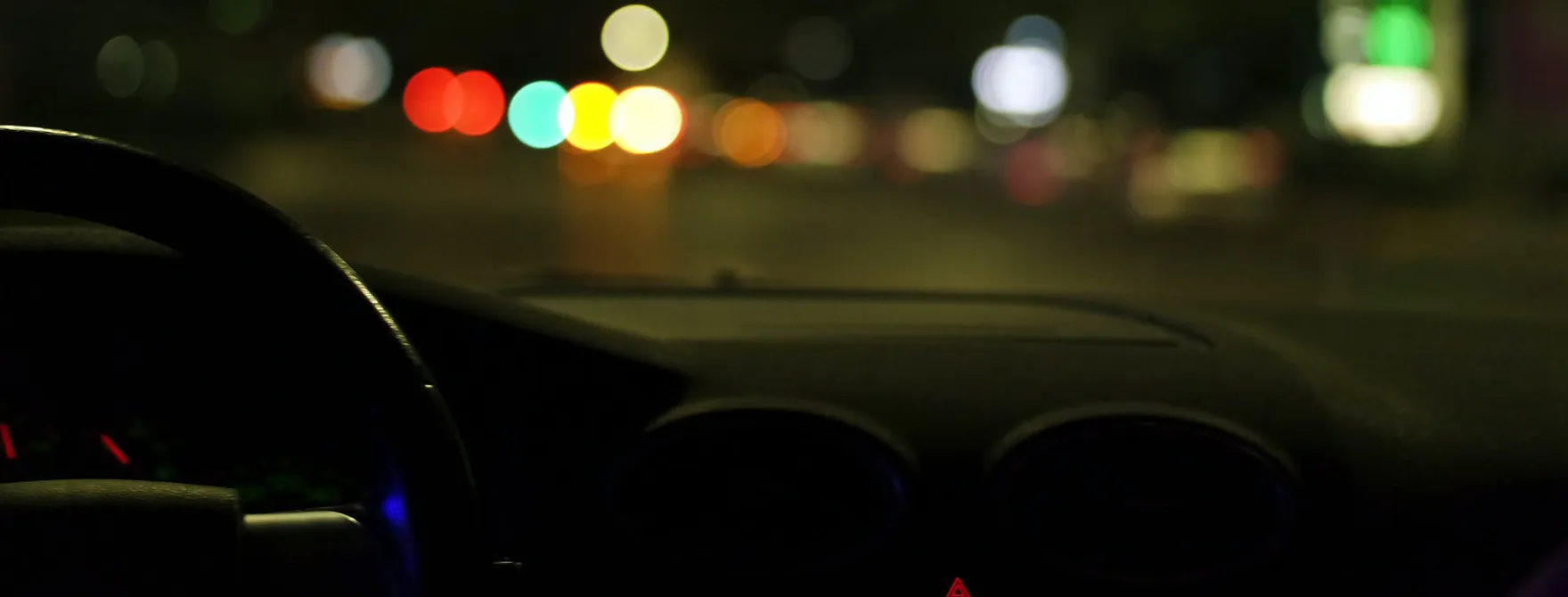 The top of a car's dashboard with blurry lights in the windshield taken at nighttime