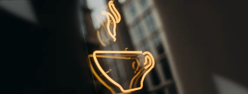 A photo of a neon coffee cup sign hanging in a window.