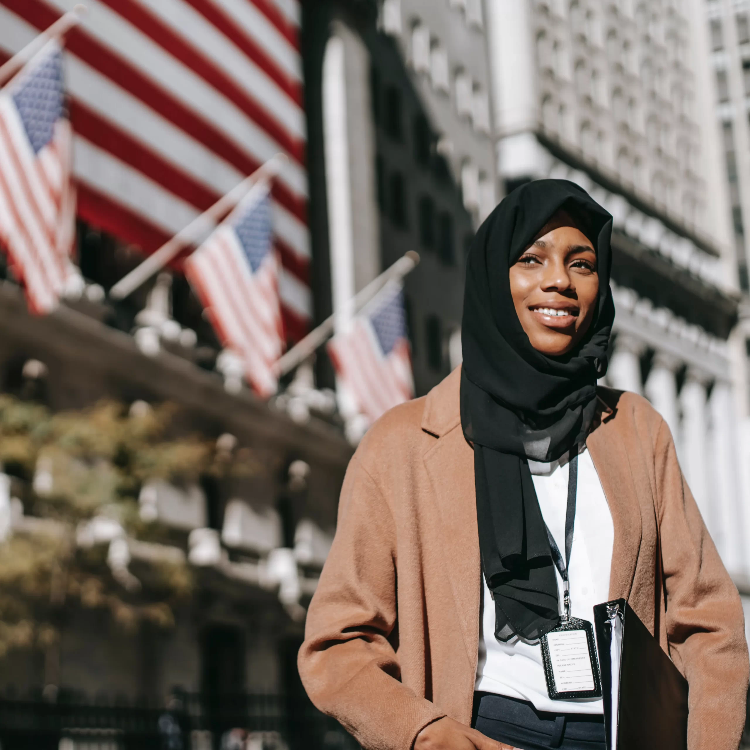 A young immigrant woman smiling outside of a building with American flags