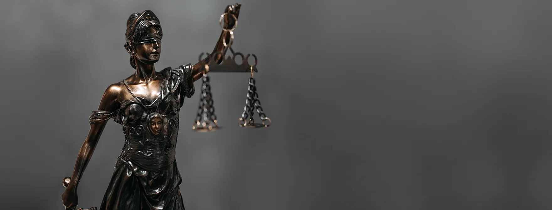 A Lady Justice statue standing in front of a blurry, gray background