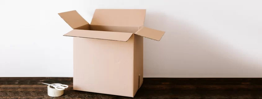 An empty moving box with a roll of packing tape and a pair of scissors next to it.