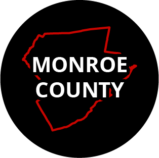 The words "Monroe County" in a black circle with red outline of the county behind it. The image links to a page listing the county's Magisterial District Courts.