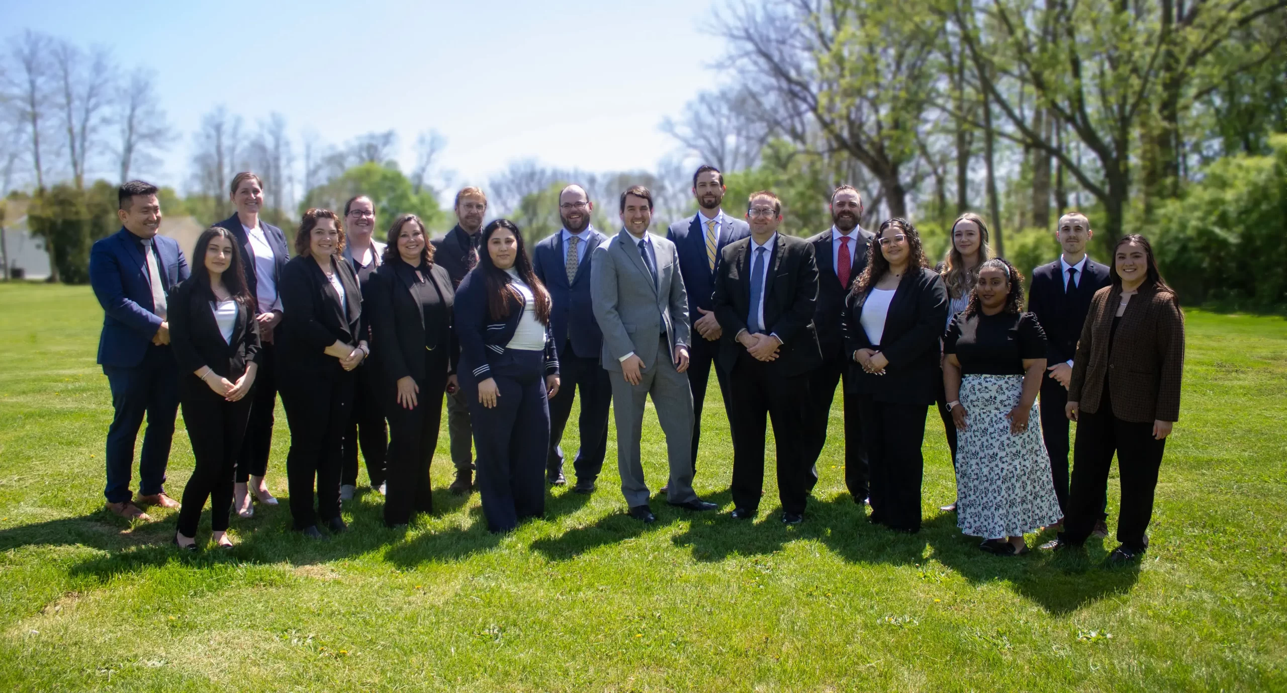 A group picture of the attorneys at staff from Cornerstone Law Firm. They're standing in a field on a sunny day.