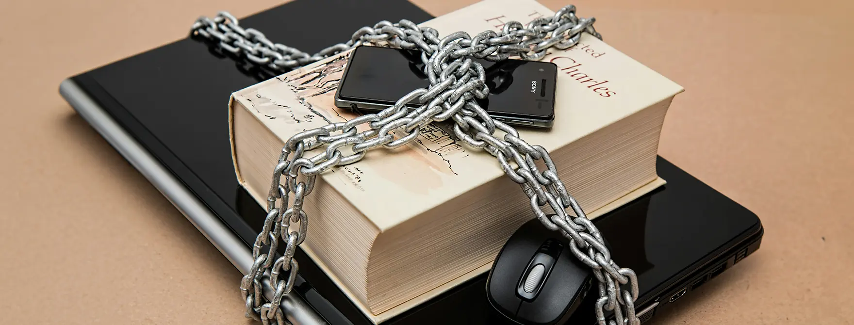 A laptop, book, and phone chained together to symbolize intellectual property protection