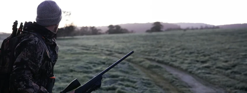 A hunter carrying a rifle and looking at a field