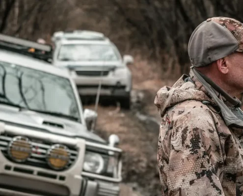 A hunter standing near some vehicles on a dirt road