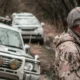 A hunter standing near some vehicles on a dirt road