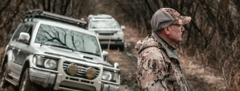 A hunter standing near some vehicles on a dirt road