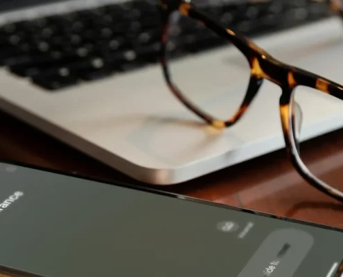 A cell phone with an incoming call from an insurance company, resting on a laptop with a pair of glasses