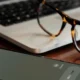 A cell phone with an incoming call from an insurance company, resting on a laptop with a pair of glasses